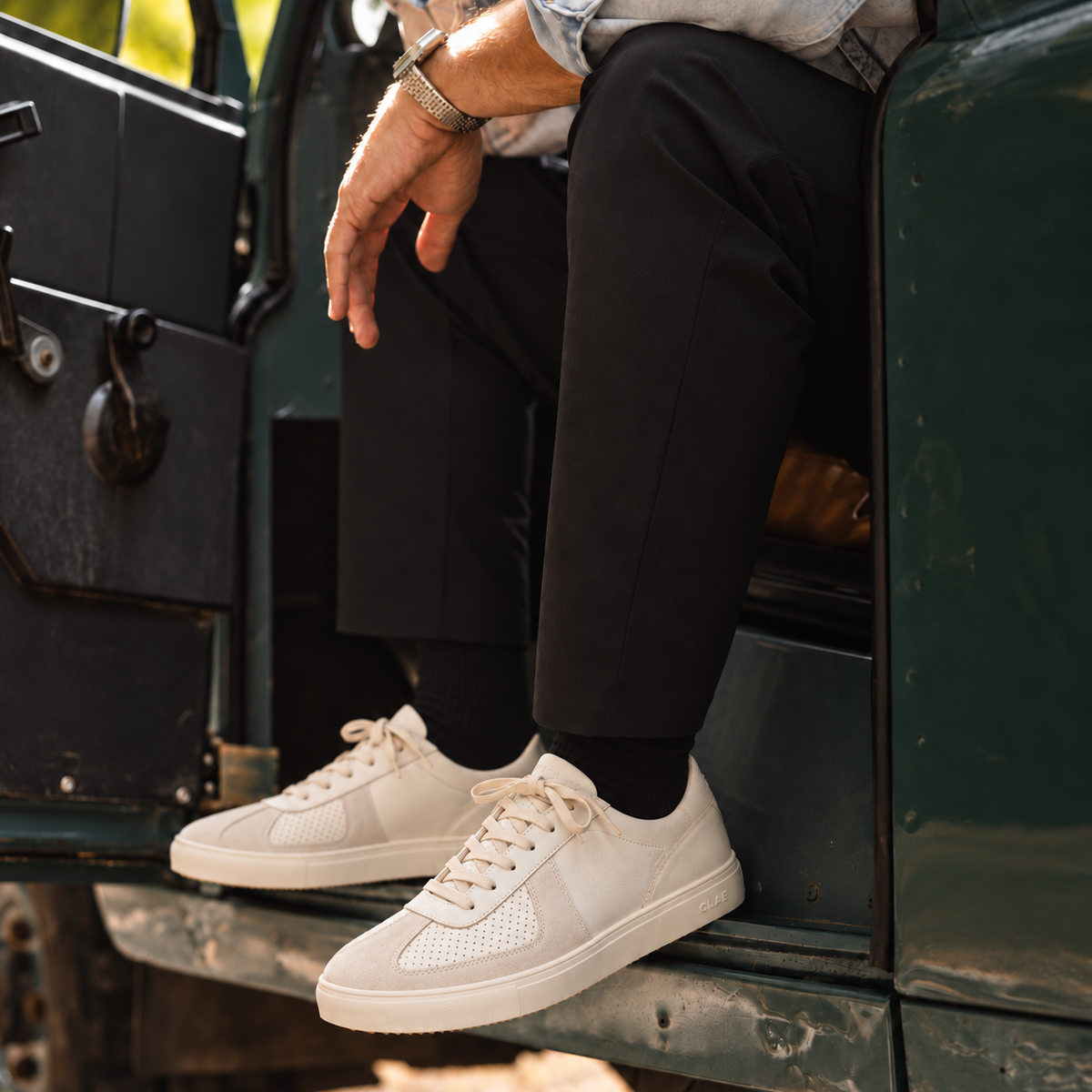 CLAE BASTIAN Triple Off-White Leather worn with dark trousers in a vintage green vehicle
